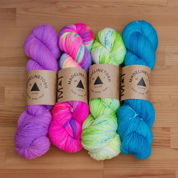 A set of purple, hot pink variegated, lime green tonal/speckled, and teal yarn.