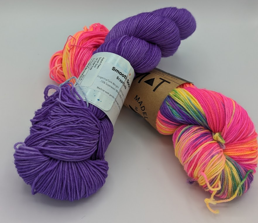 Two skeins of yarn, a mid-toned purple stacked on top of the variegated pink from earlier.